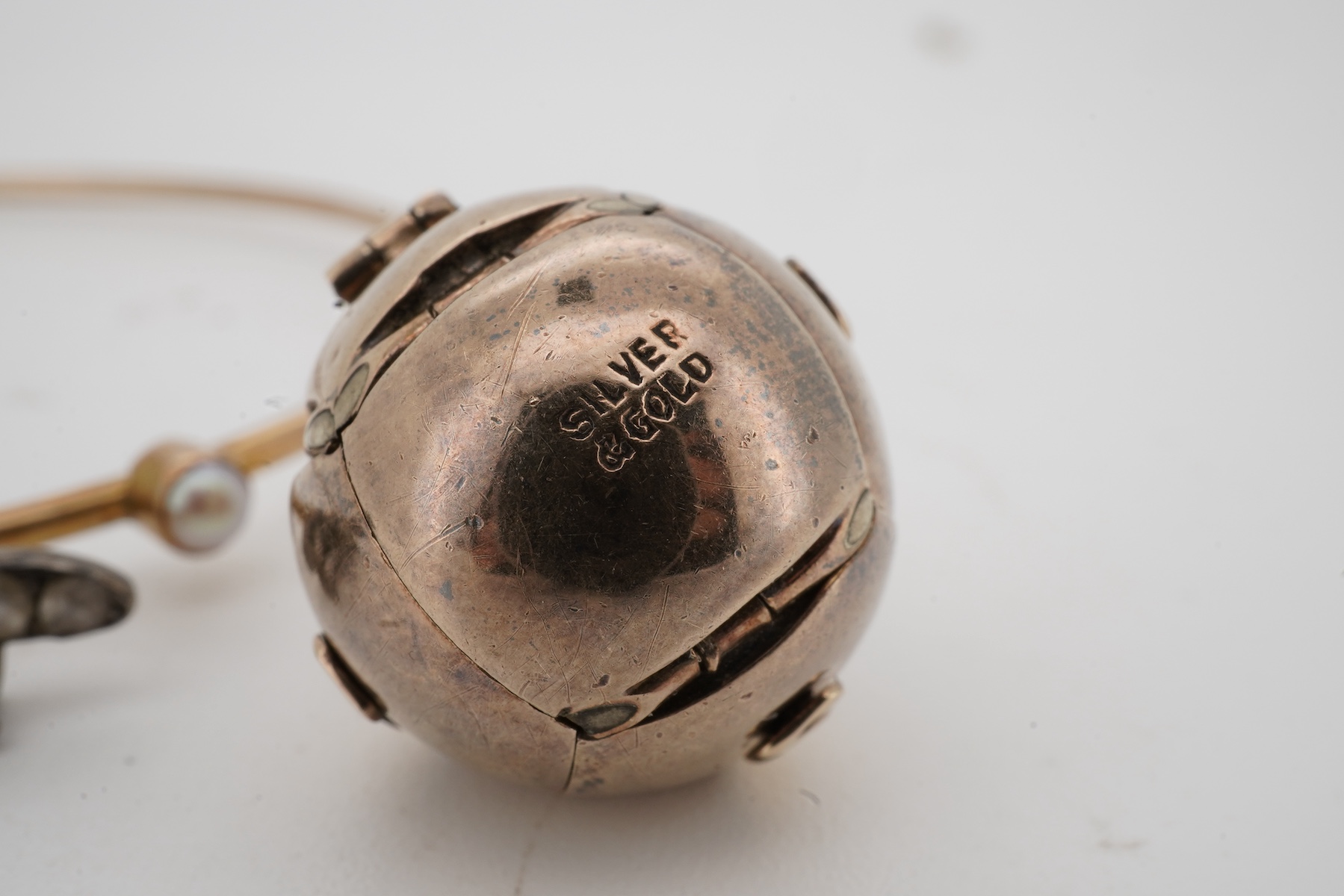 A Masonic ball pendant and a pearl and diamond bangle, early 20th century, the Masonic ball folding open to reveal a cross shape engraved with Masonic symbols, in gilt silver, length 2.2cm when closed, stamped Silver & G